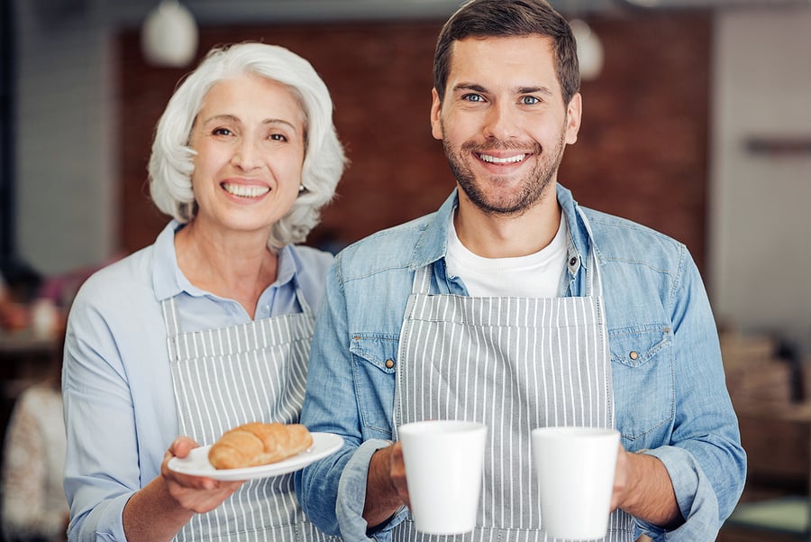 Two generations of a bakery family holding coffee and pastries