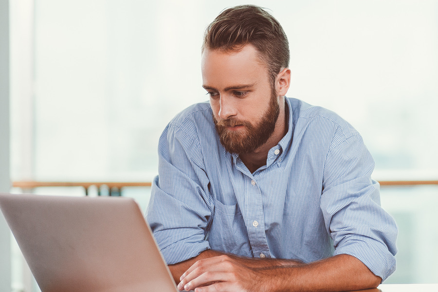 Bearded man focused on his laptop screen at a desk