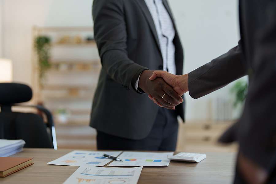 Two colleagues shaking hands over a desk with paperwork