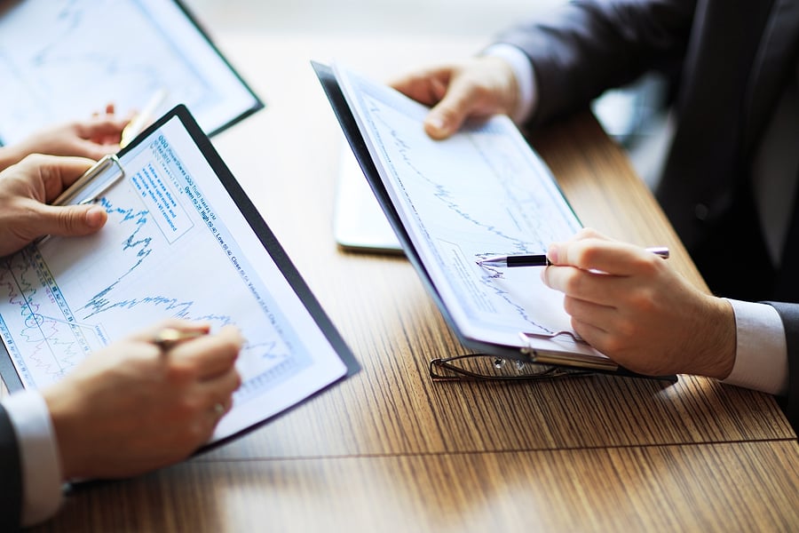 Two people comparing financial charts on clipboards