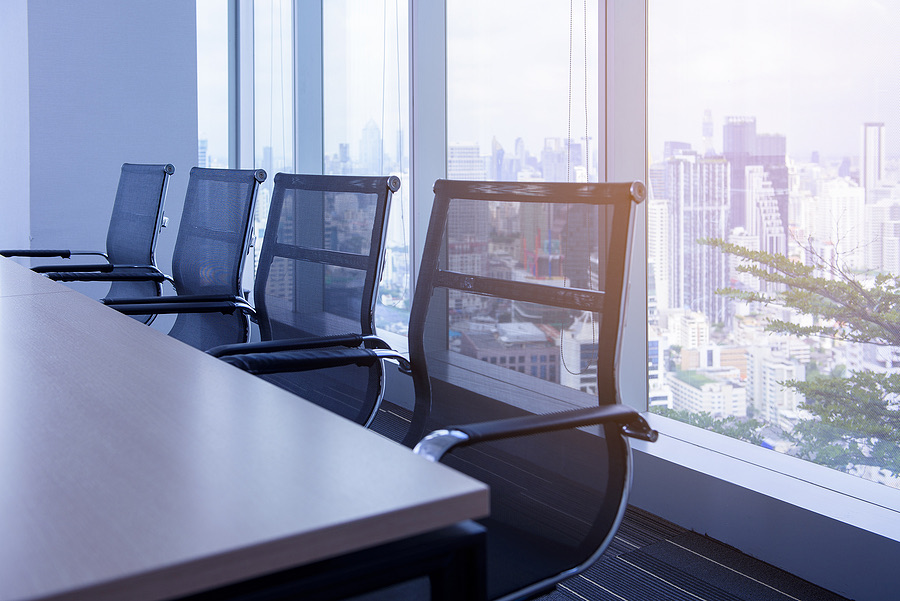 Empty conference room chairs facing floor-to-ceiling city view windows