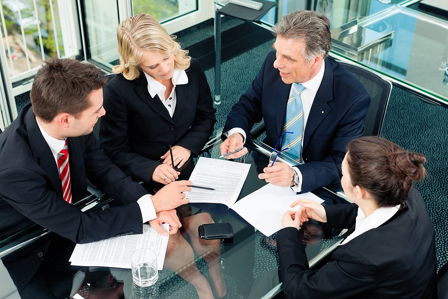 Four colleagues reviewing and signing paperwork around a glass table