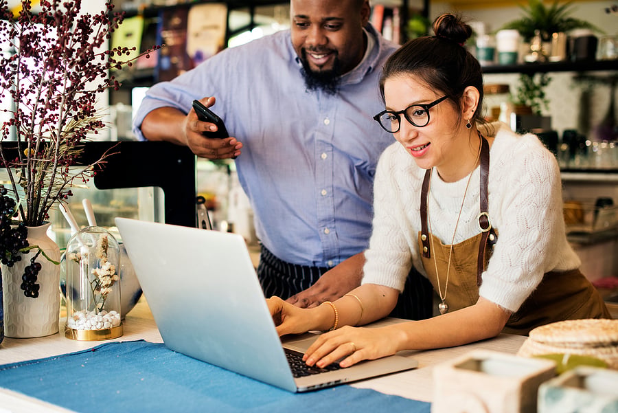 Small business owner and colleague reviewing a laptop at the counter