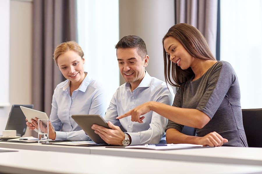 Three colleagues smiling while reviewing a tablet together