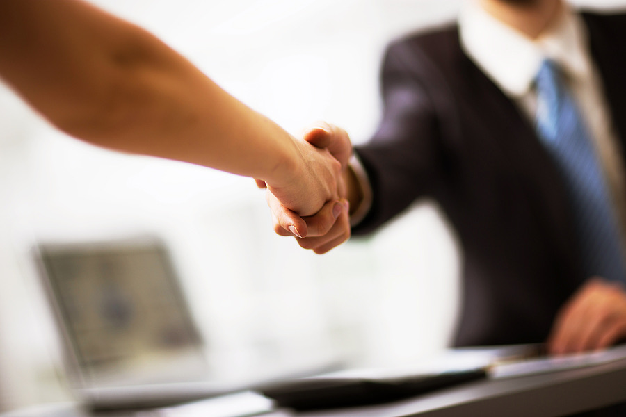 Close-up handshake between two colleagues with a laptop nearby