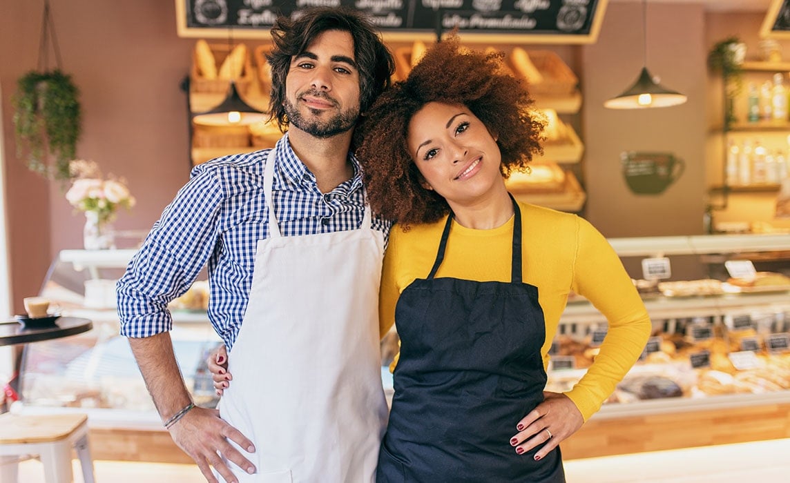 Two small-business owners in aprons standing in their bakery