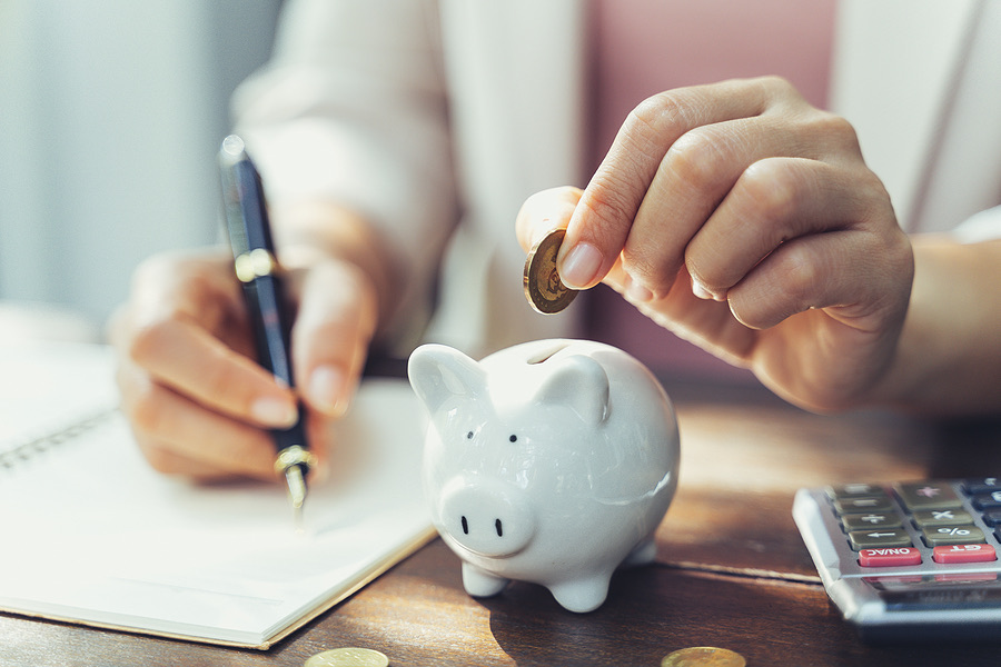 Hands placing a coin into a piggy bank beside a calculator