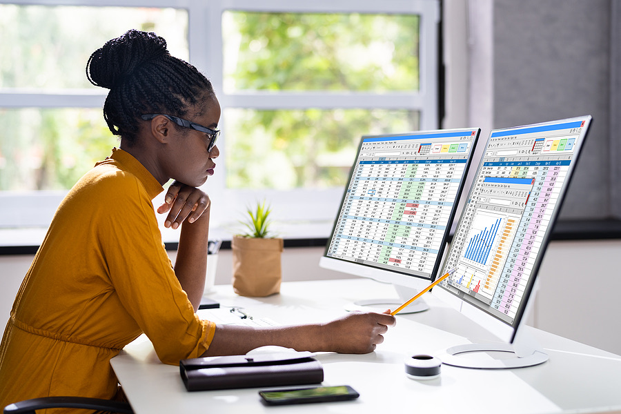 Businesswoman analyzing spreadsheet data on dual monitors