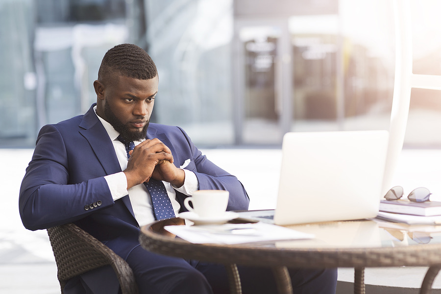 Businessman looking concerned while working at a laptop outdoors