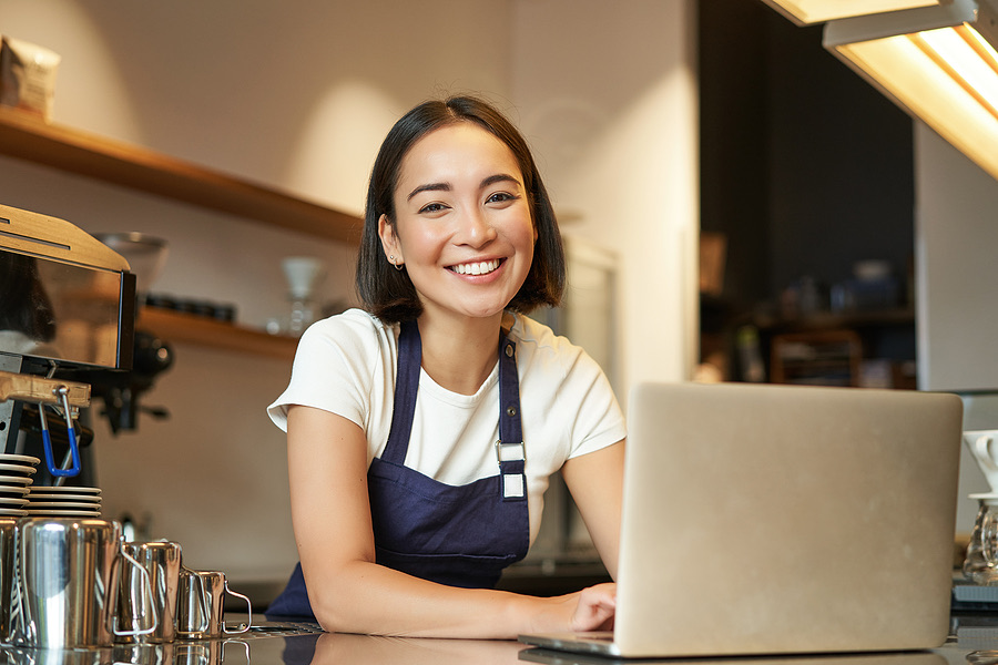 Smiling cafe owner leaning on the counter beside a laptop