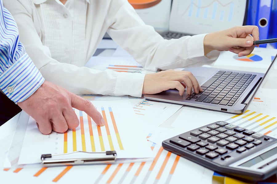 Two colleagues reviewing financial charts beside a laptop and calculator