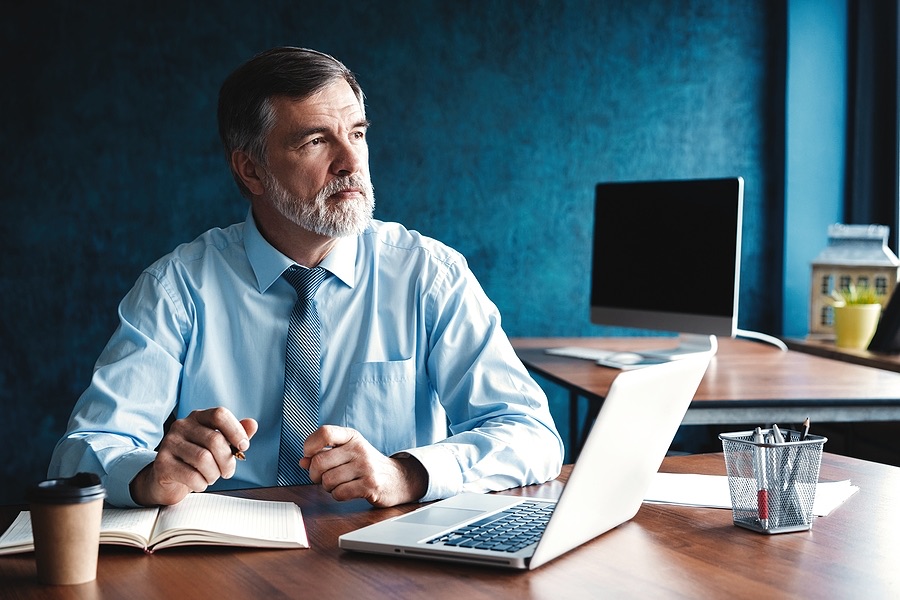 Business owner sitting at a desk with a laptop, lost in thought