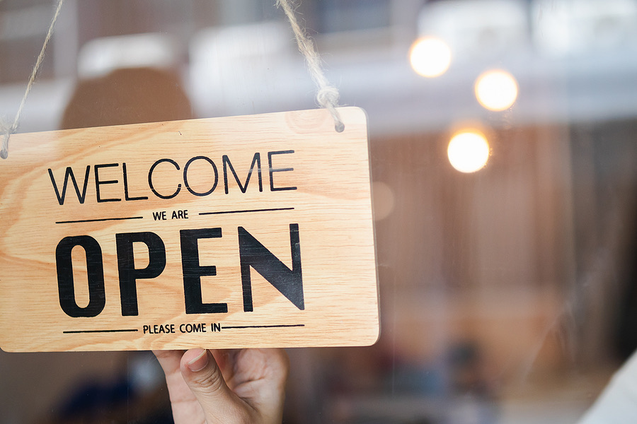 Hand holding a wooden welcome and open sign in a shop window