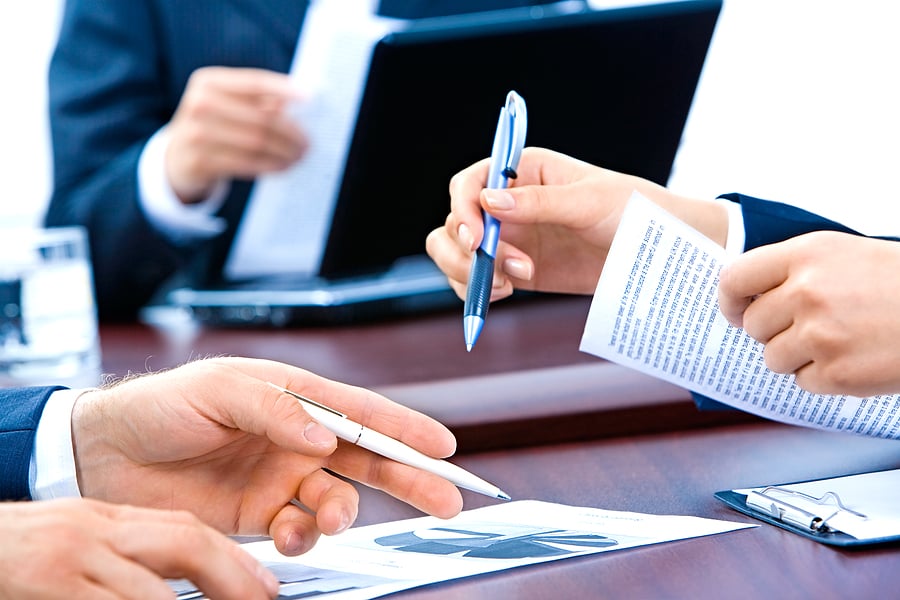 Colleagues' hands exchanging documents and pens at a meeting table