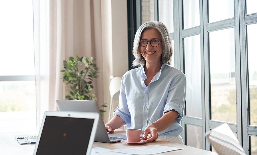 Smiling business owner sitting at a desk with coffee and a laptop