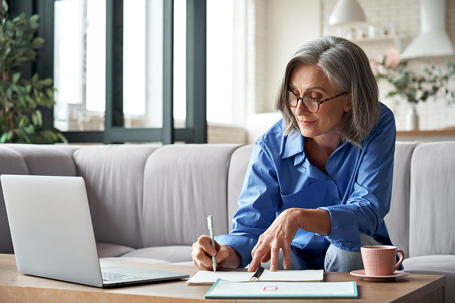 Business owner writing notes beside a laptop on a coffee table