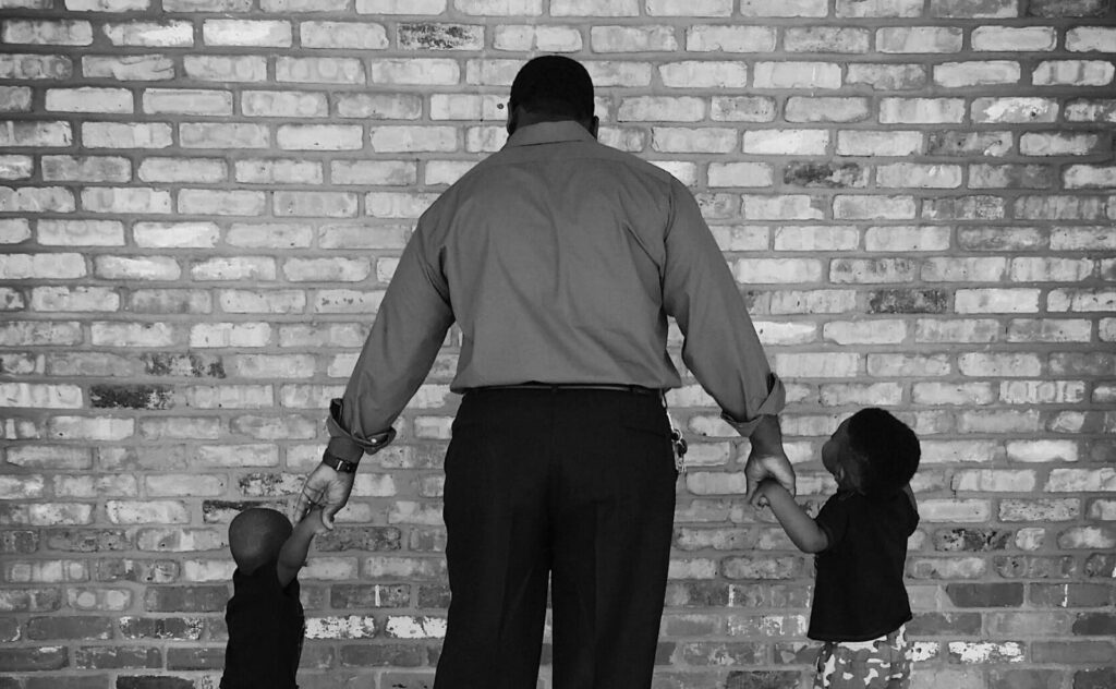Parent holding hands with two children by a brick wall
