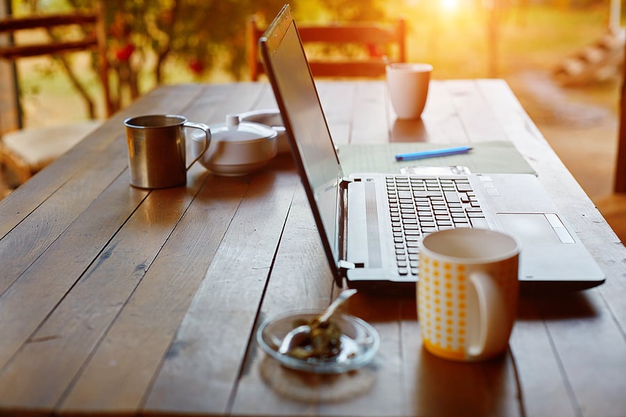 Laptop and coffee mugs set on an outdoor wooden table