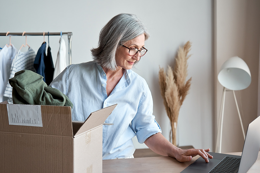 Shop owner working at a laptop beside a box of clothing