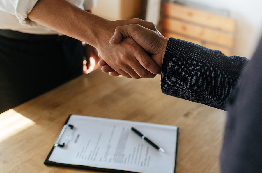 Two people shaking hands over a clipboard on a desk