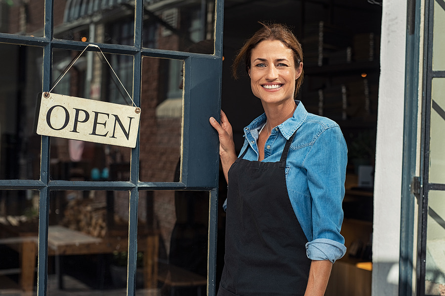 Smiling shop owner holding open the door under an open sign