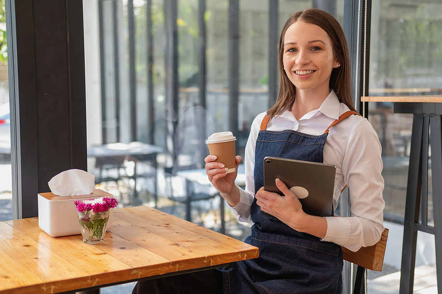 Cafe worker in an apron holding a coffee cup and tablet