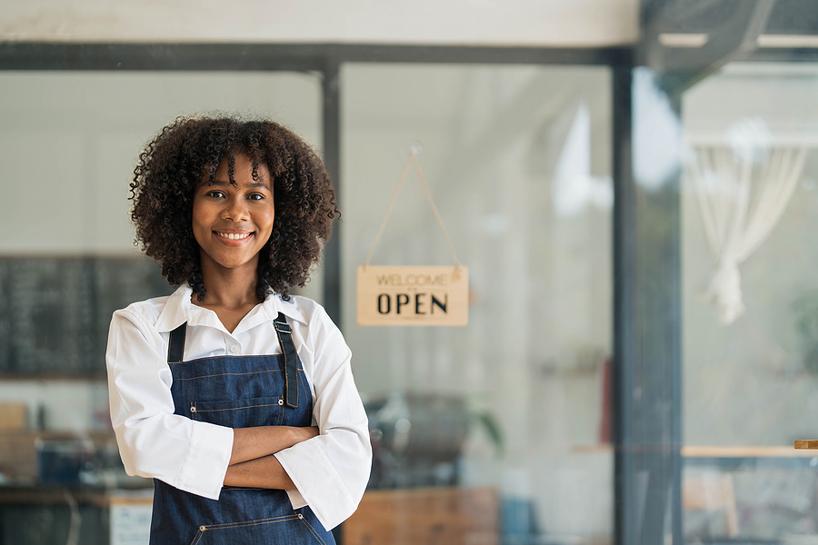 Shop owner smiling with arms crossed by an open sign