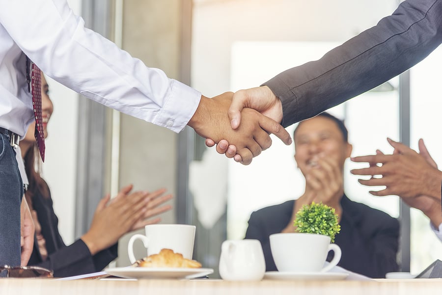 Two people shaking hands as colleagues applaud at the table