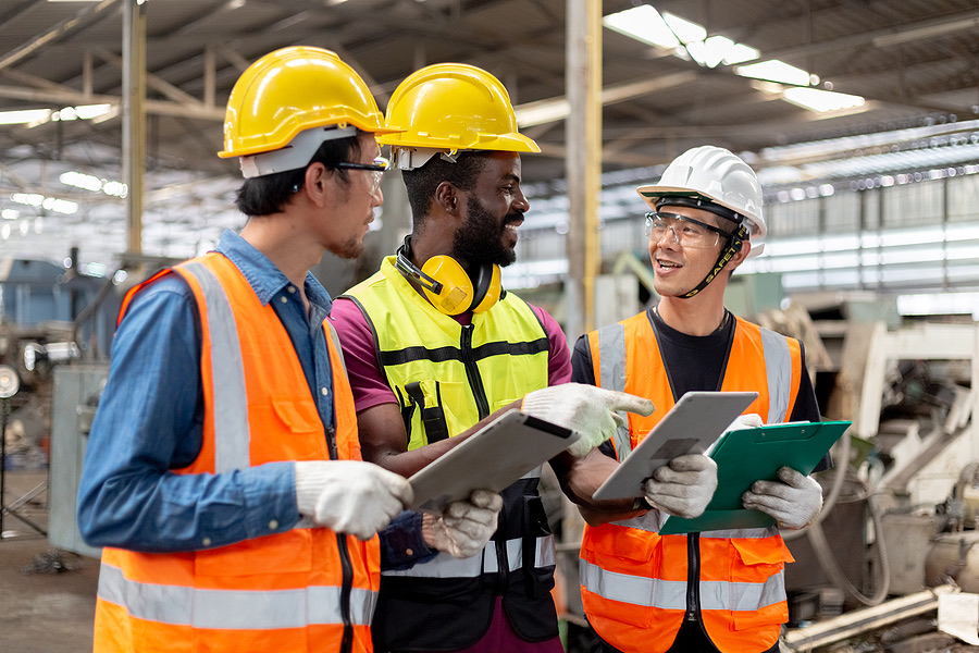 Three industrial workers reviewing plans on a factory floor