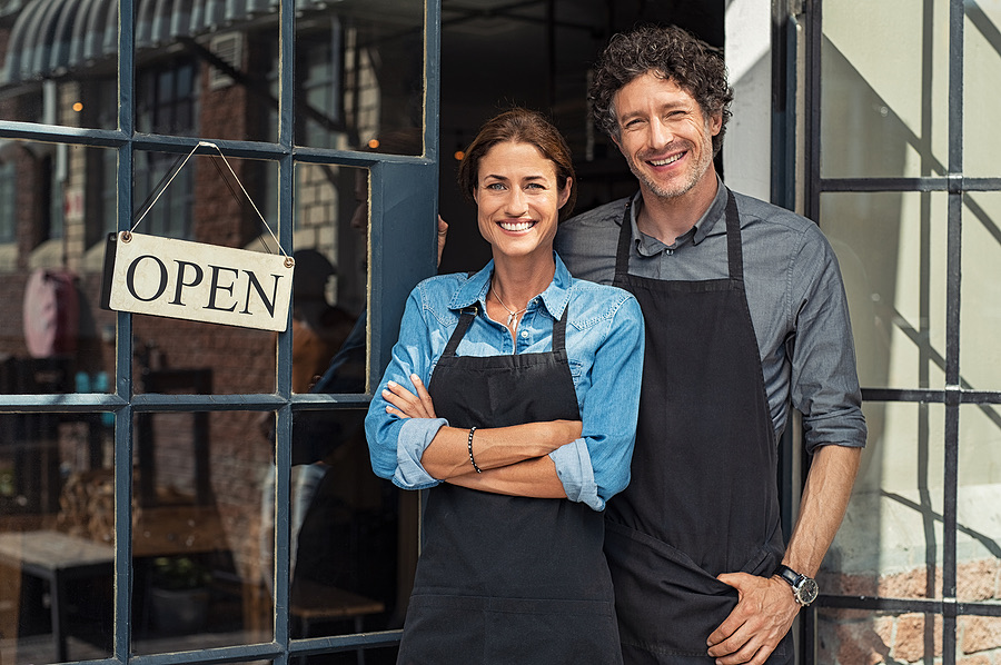 Two smiling small business owners standing at their shop entrance