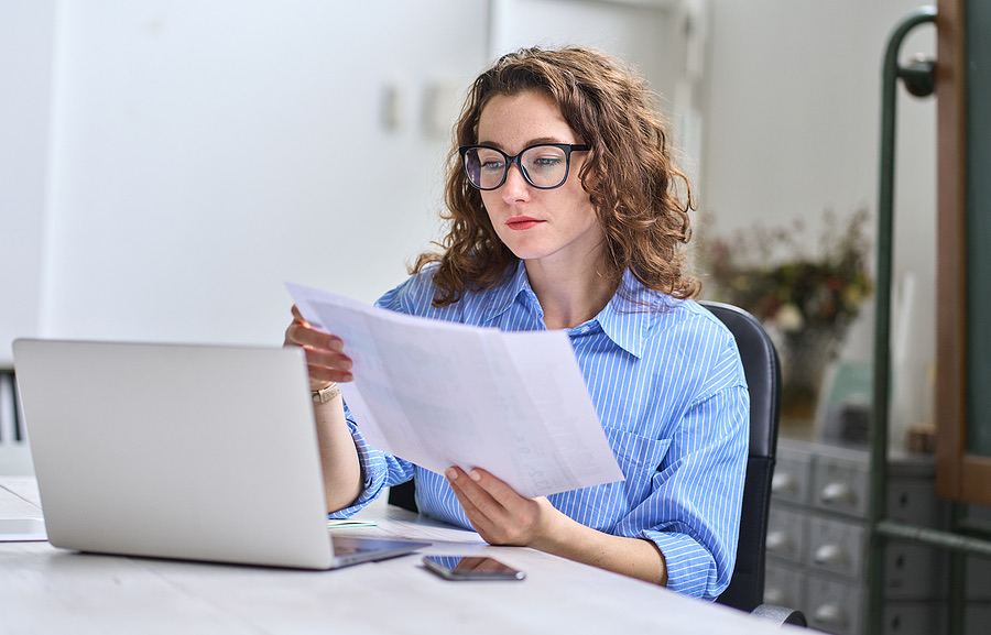 Business owner reviewing a paper document at her laptop