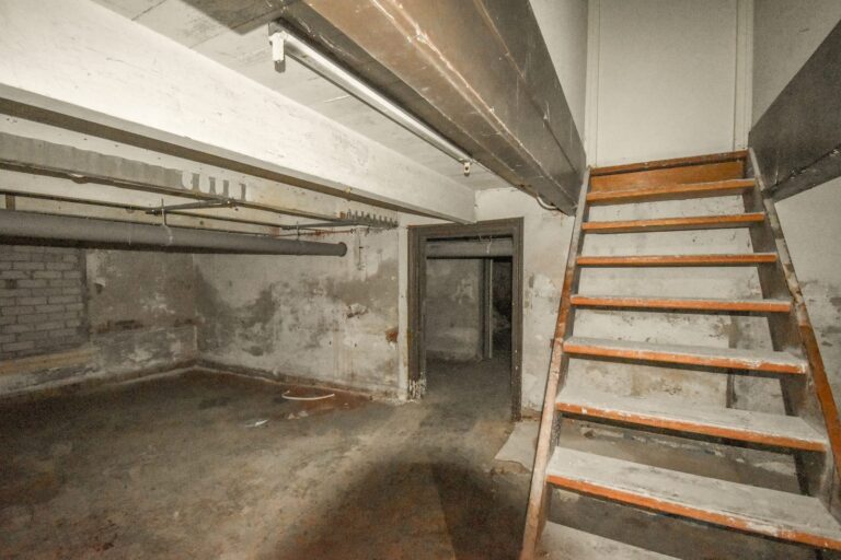 Unfinished basement with concrete walls and wooden stairs